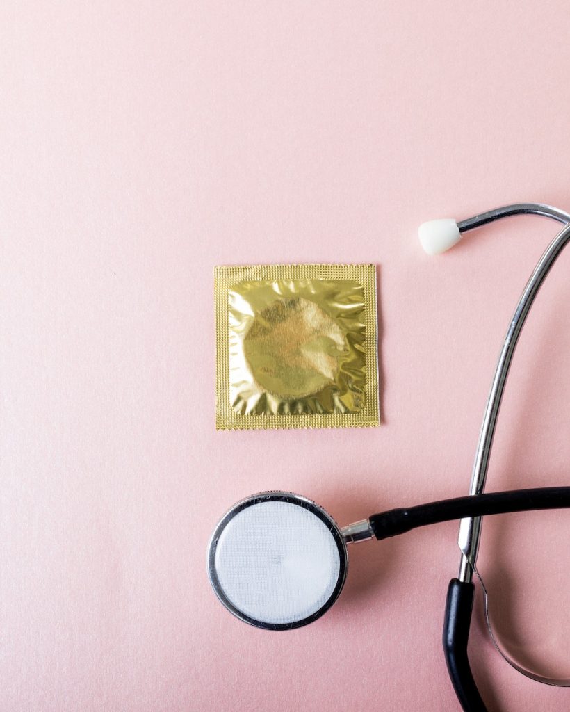 Directly above shot of stethoscope with condom in pack against pink background, copy space